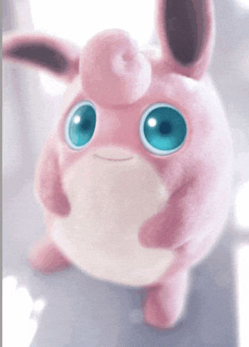 a pink stuffed animal with blue eyes is looking up at the camera