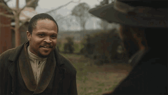 a man in a suit and hat talks to another man