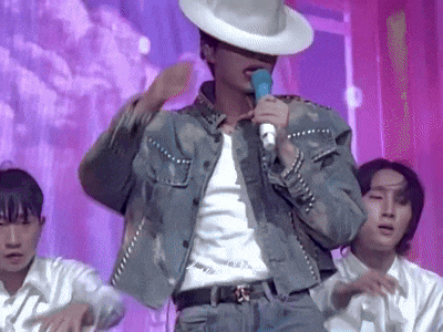 a man in a cowboy hat is singing into a microphone while wearing a denim jacket .
