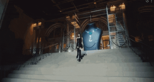 a woman stands on a set of stairs in front of a large statue