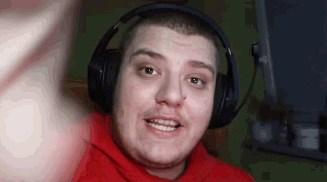 a man wearing headphones and a red hoodie is smiling and looking at the camera .