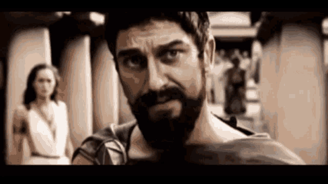 a man with a beard is looking at the camera with a woman in the background .