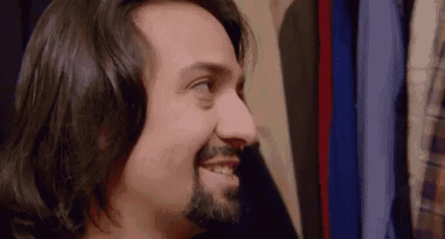 a man with long hair and a beard is smiling while standing in front of a closet .