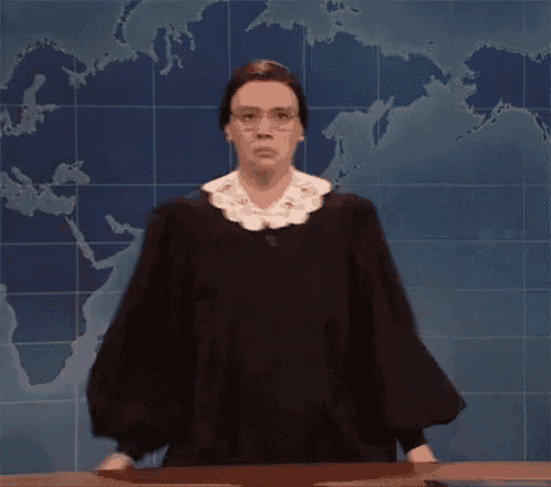 a woman in a judge 's robe and glasses is standing in front of a map of the world .