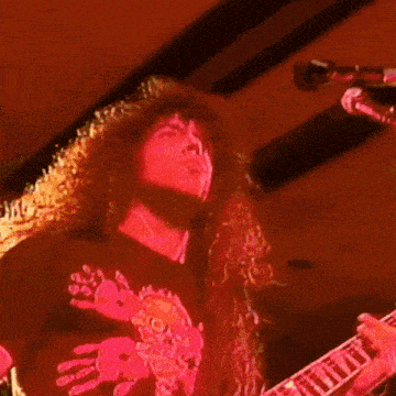 a man with long curly hair is playing a guitar and singing into a microphone .
