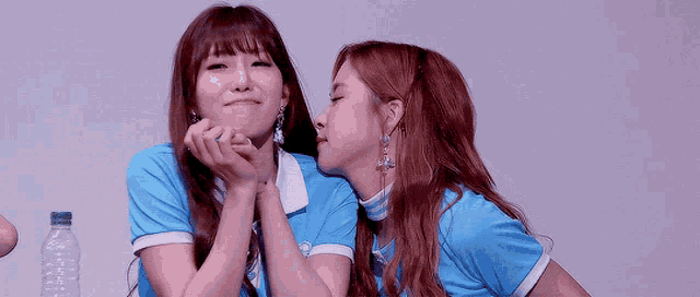 a woman kissing another woman on the cheek in front of a bottle of water