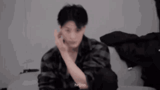 a blurry picture of a man sitting on a couch with his hand in his ear .
