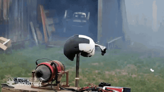 a black and white helmet is sitting on a stand in front of a sign for hacksmith industries