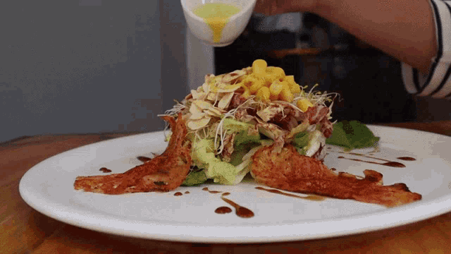 a plate of food with a person pouring dressing on it