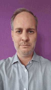 a man with a beard wearing a gray shirt against a purple background