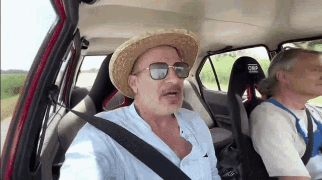 a man wearing a straw hat and sunglasses is sitting in a car with another man .