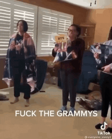 a group of people are standing in a room holding albums and a sign that says `` fuck the grammys '' .