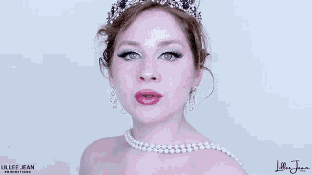 a woman is wearing a tiara and a pearl necklace and smiling .