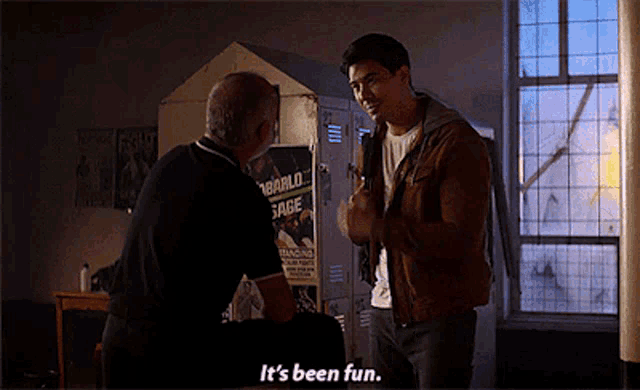 a man talking to another man in front of a locker with a poster that says " it 's been fun " on it