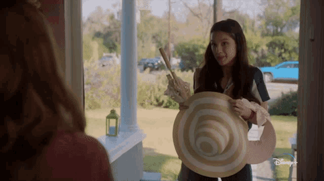 a girl is holding a large hat in front of a door that says disney plus