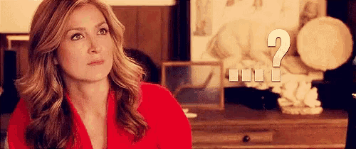 a woman in a red jacket is sitting in front of a desk with a question mark .