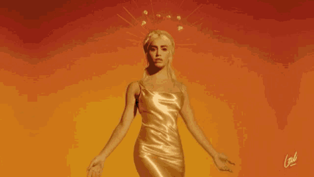 a woman in a gold dress with a crown on her head is standing in front of a fire .