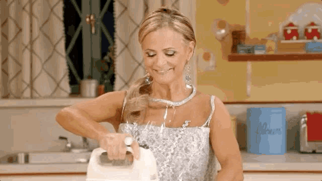 a woman in a dress is using a mixer in a kitchen and smiling .