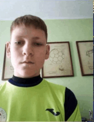 a young boy in a green shirt is looking at the camera in front of a green wall .