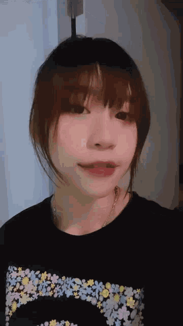 a woman wearing a black shirt with flowers on it looks at the camera