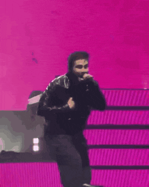 a man is standing on a stage with his hands on his chest and a purple background .