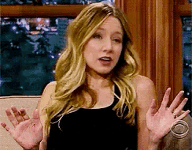 a woman in a black dress is sitting on a couch with her hands in the air .