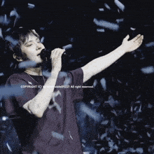 a man in a purple shirt singing into a microphone while confetti falls around him
