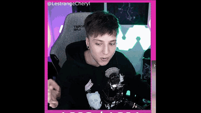 a man is sitting in a gaming chair and talking into a microphone while wearing a black hoodie