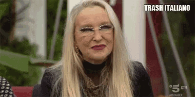 a woman with blonde hair and glasses is making a funny face while sitting on a chair .