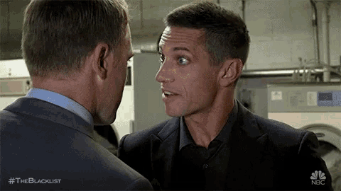 two men are standing next to each other in a laundromat and talking to each other .