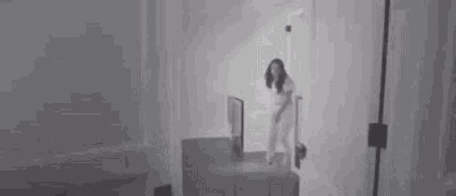 a woman in a white shirt is standing in a dark room in a black and white photo .