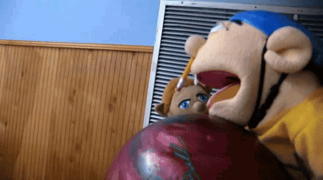 a stuffed animal with a pencil in its mouth is holding a bowling ball