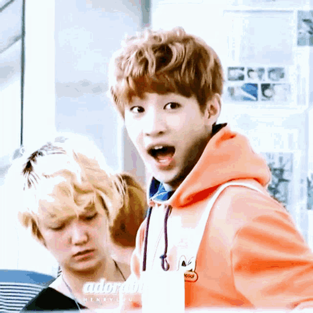 a boy with a surprised look on his face is wearing an orange hoodie that says adorable