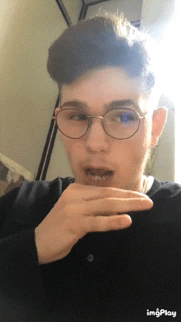 a young man wearing glasses and a black shirt is making a face