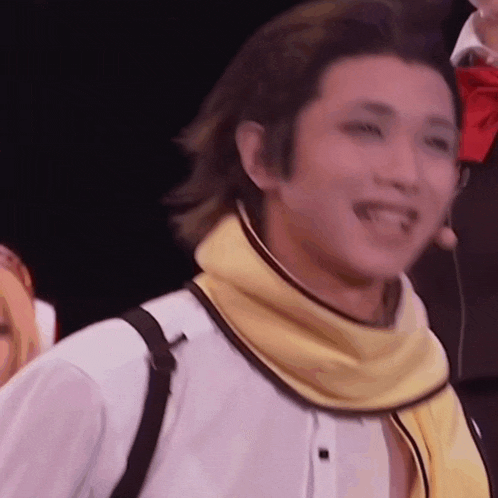 a man wearing a white shirt and a yellow scarf is smiling on stage .