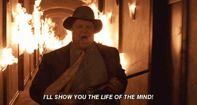 a man holding a gun says i 'll show you the life of the mind in front of a fire
