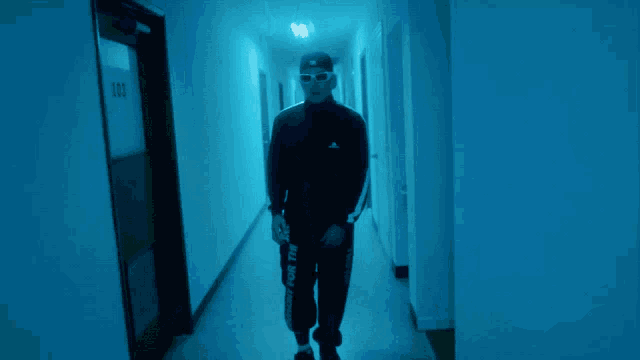 a man wearing a hat and sunglasses is walking down a hallway
