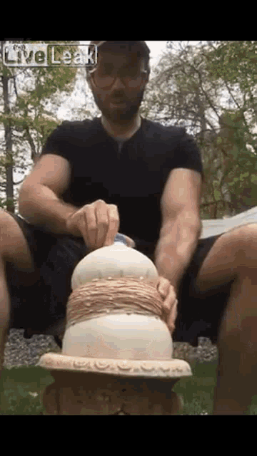 a man in a black shirt is sitting on a bench with a cake in front of him and the words live leak on the bottom right