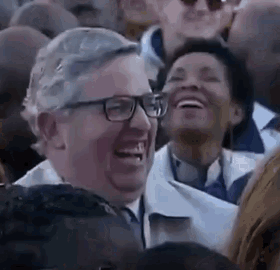 a man wearing glasses is laughing in a crowd .