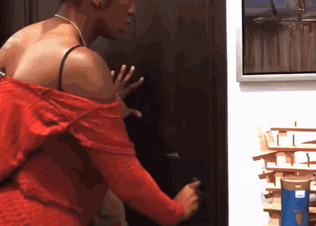 a woman in a red dress is opening a door with her hand