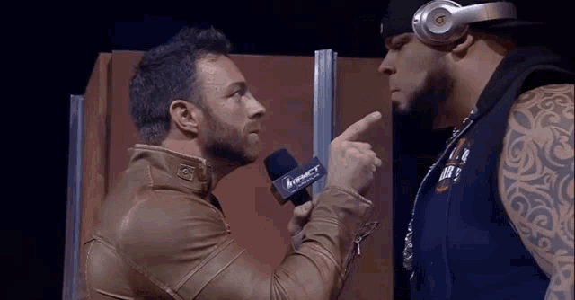 a man wearing headphones is pointing at another man wearing a microphone that says impact on it .
