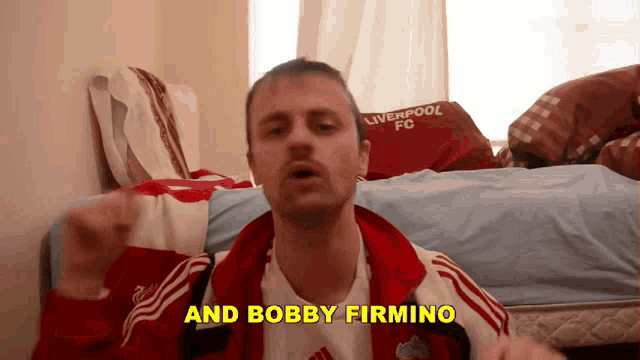 a man wearing a liverpool fc shirt stands in a bedroom