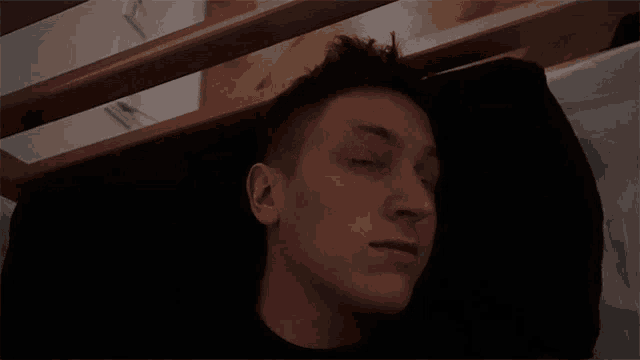 a young man is sleeping on a bed with his eyes closed .