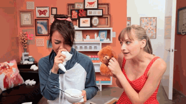 a woman blows her nose while another woman holds a stuffed animal