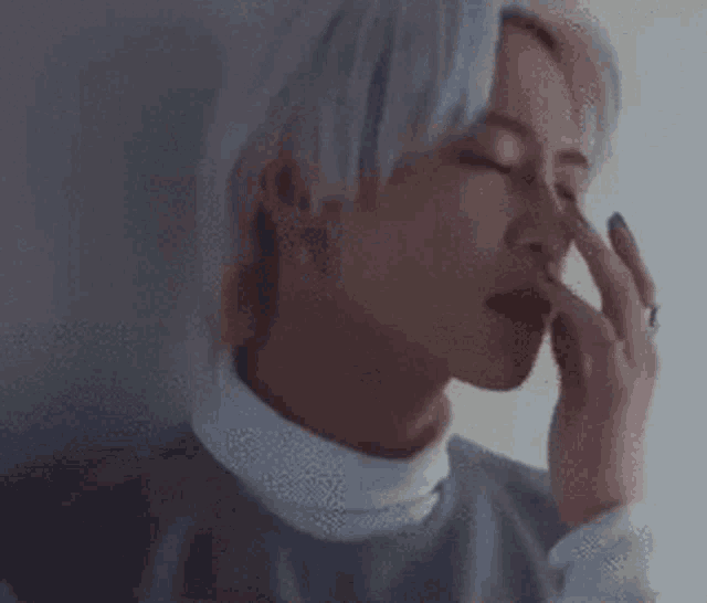 a close up of a person 's face with their eyes closed and their hand on their nose .
