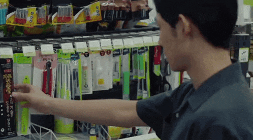 a man is standing in front of a shelf in a store looking at a pen .