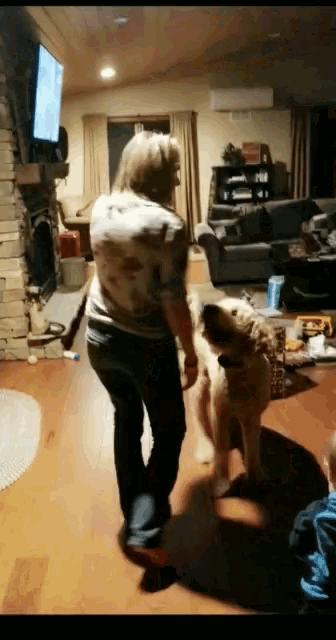 a woman is standing in a living room playing with a dog