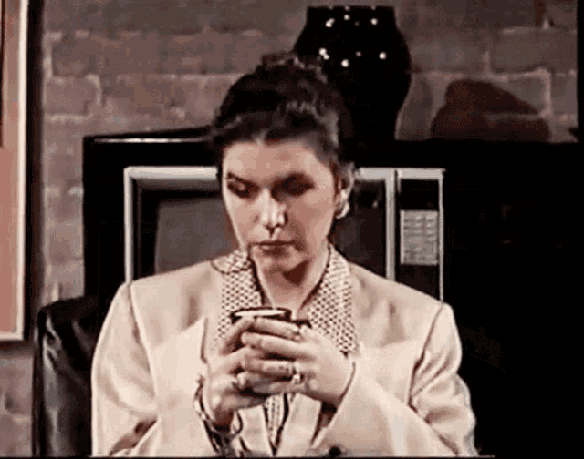 a woman in a tan suit is holding a cup of coffee