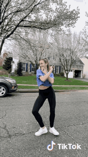 a woman is dancing in front of a house with a tik tok logo on the bottom