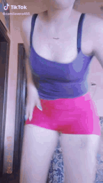 a woman in a purple tank top and pink shorts is standing in a room .